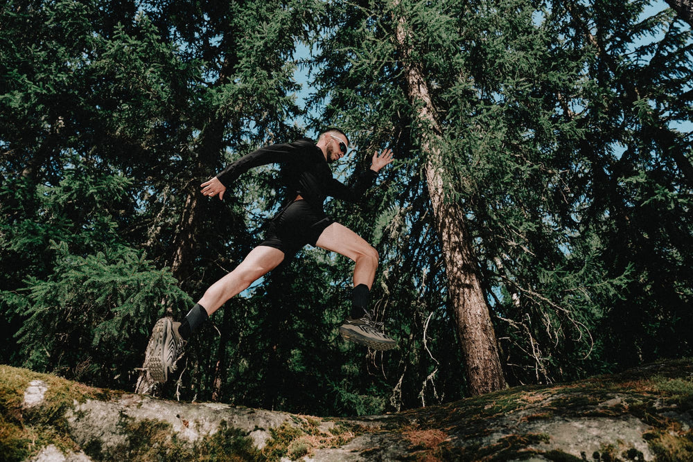 Coureur en trail running sautant sur un sentier en forêt avec équipement technique de trail